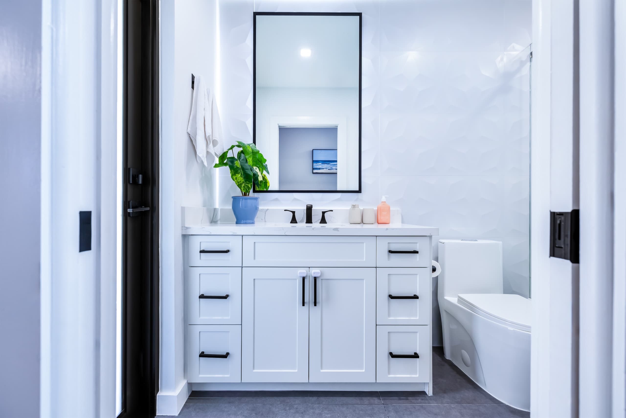 Bathroom vanity with a black-framed mirror and a black faucet, seen through the doorway.