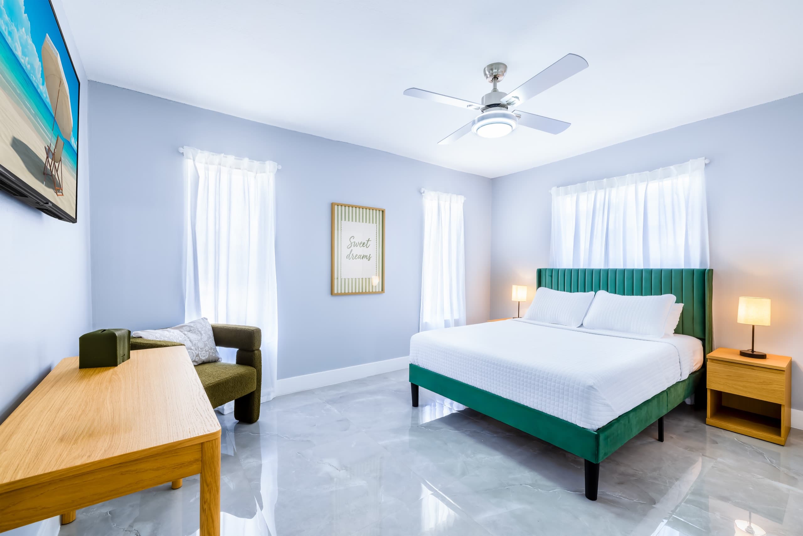 Bedroom with the emerald bed, windows with white curtains, a ceiling fan and an armchair.