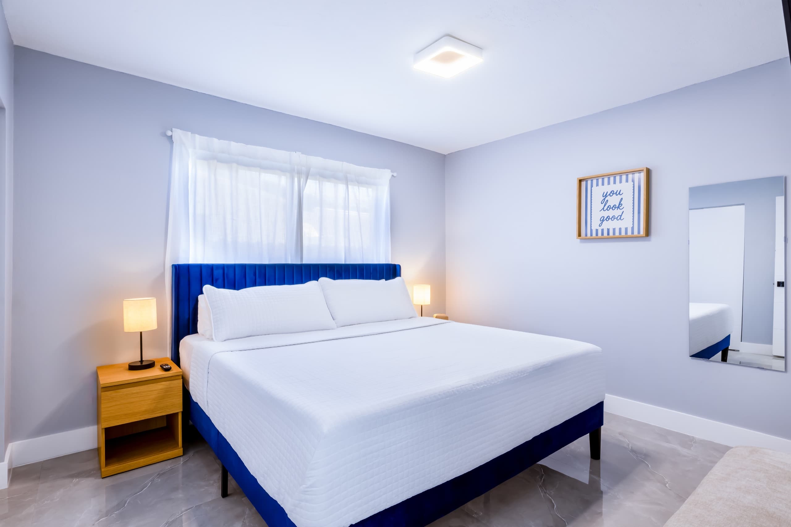 King bed with a cobalt upholstered headboard and white bedding under a window, with lamps lit on oak nightstands.