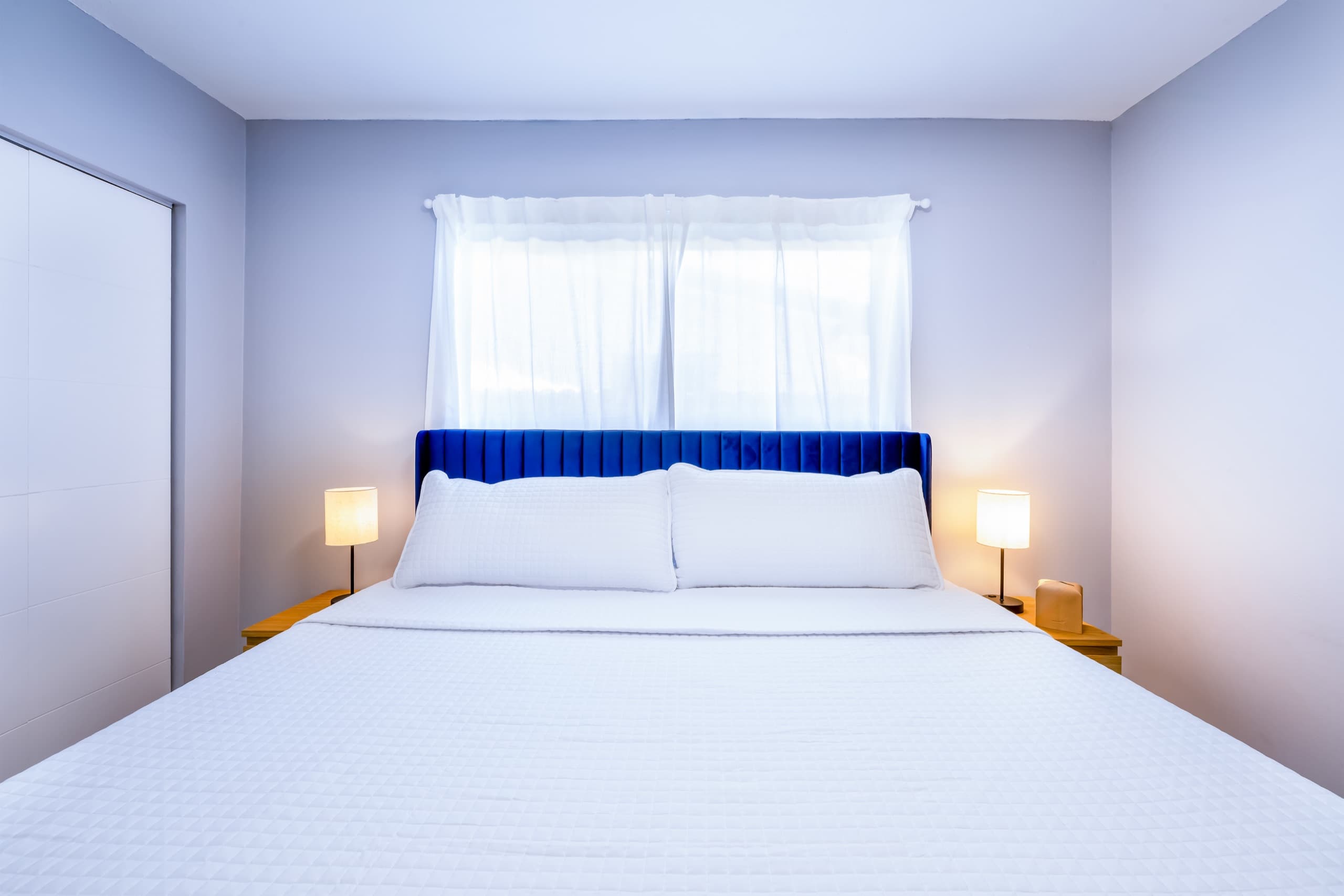 Cobalt headboard centred under a window, with matching lamps on both sides.