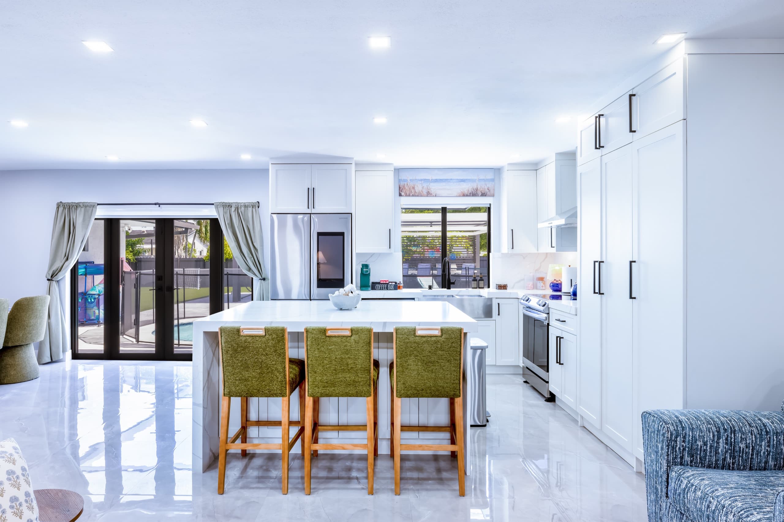 Kitchen island with three green bar stools, with glass doors to the pool on the left.