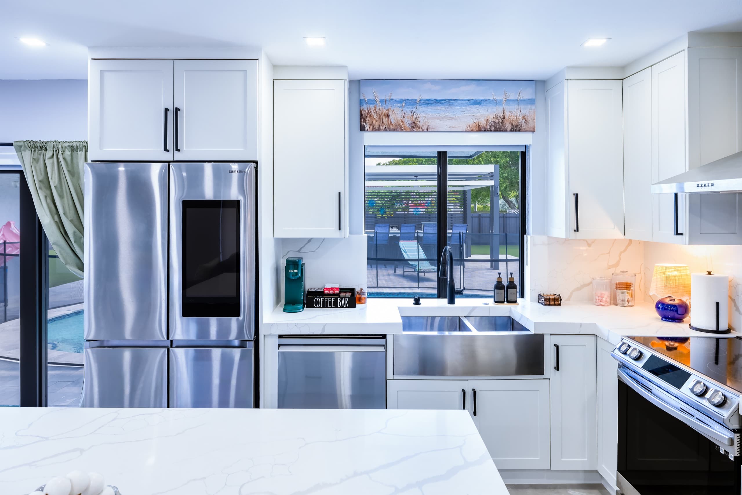Kitchen sink under a window that looks out to the outdoor kitchen, with the refrigerator and dishwasher to the left.