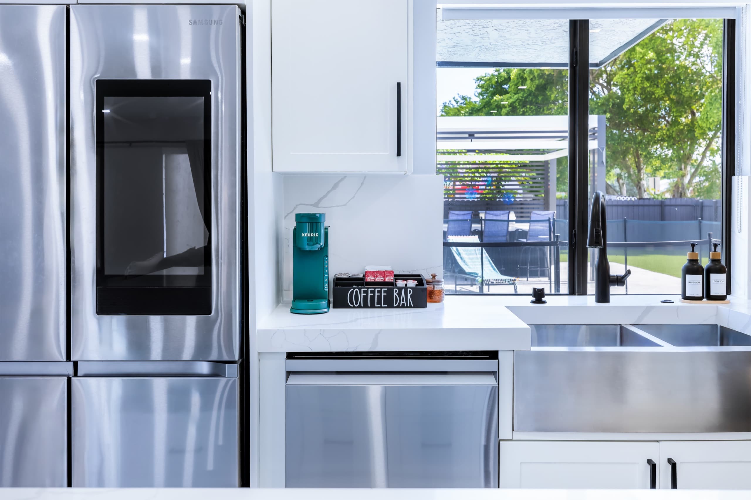 Coffee maker and coffee pods on the counter beside the refrigerator and the sink.