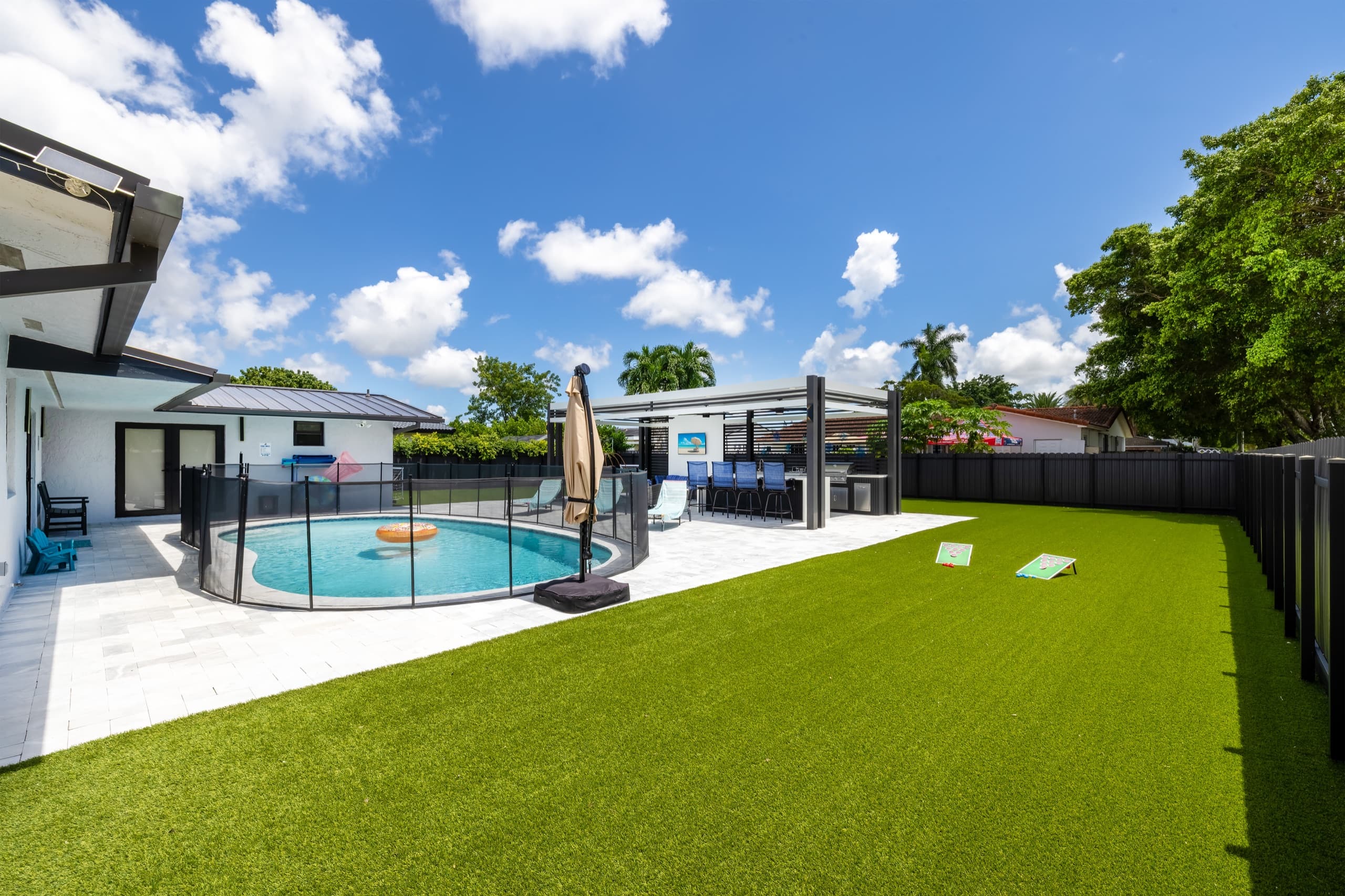The backyard in daylight: the house, the fenced pool, the pavilion and the lawn.