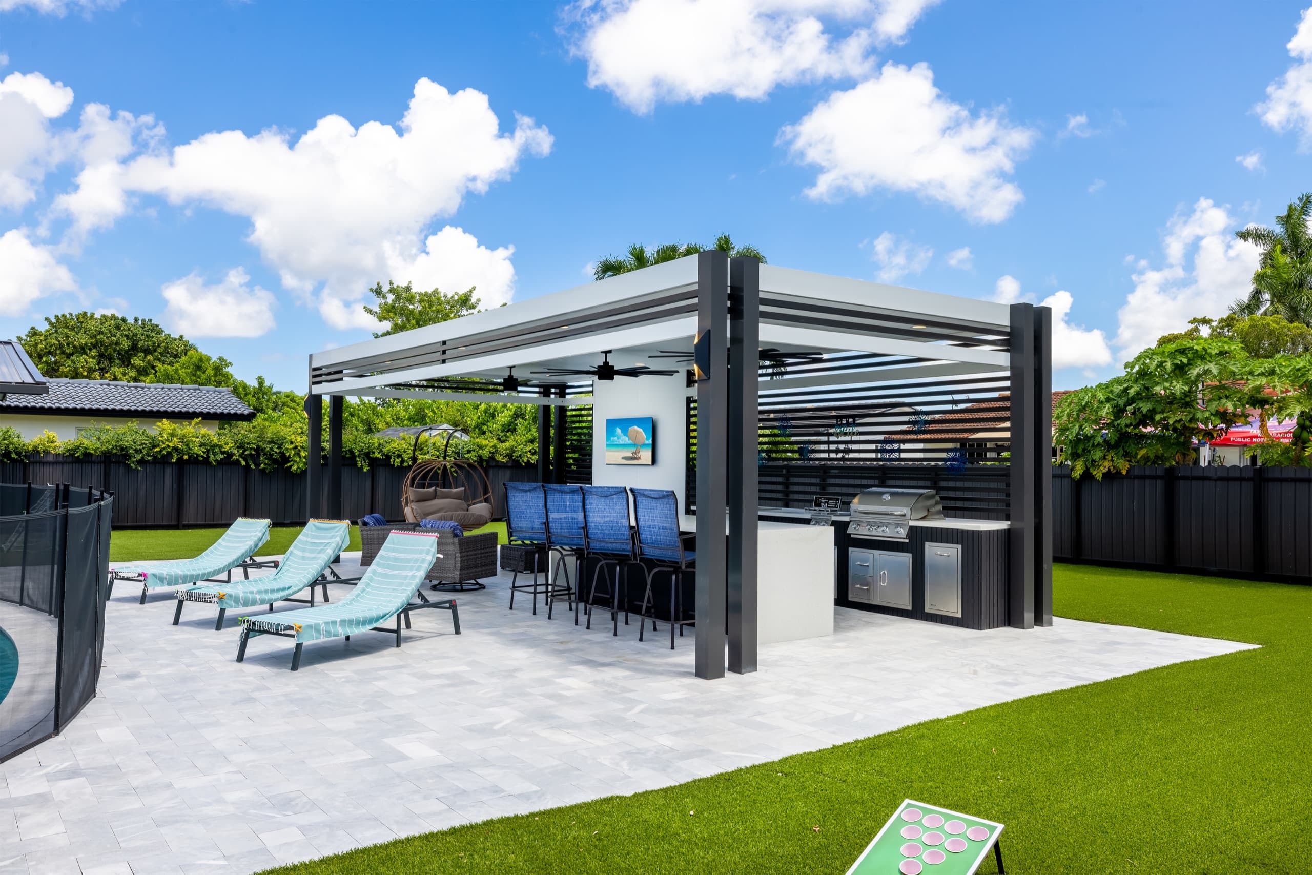 The pavilion with bar stools, grill and loungers on a stone deck in daylight.
