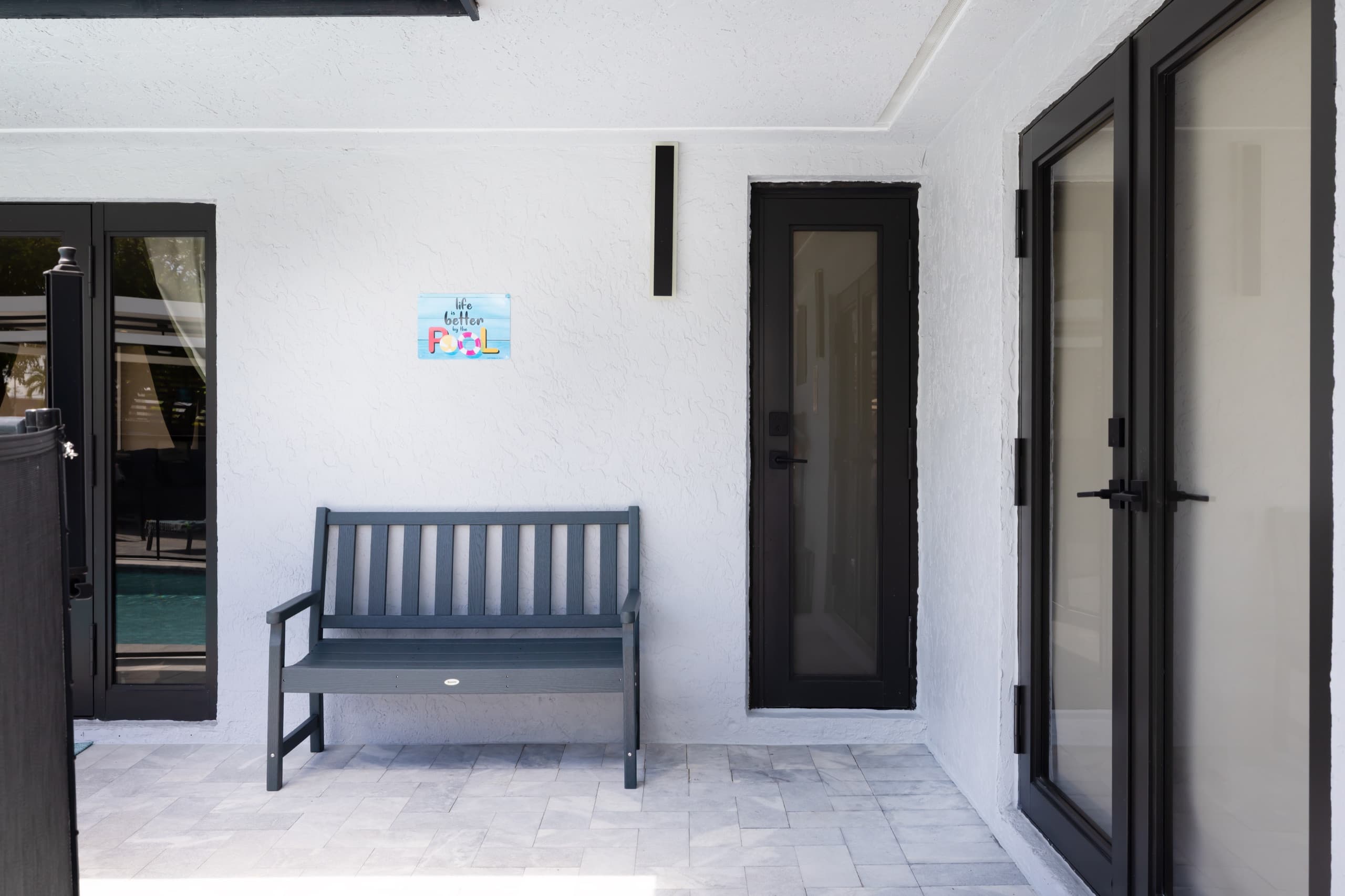 Covered porch wall with a bench and glass doors.