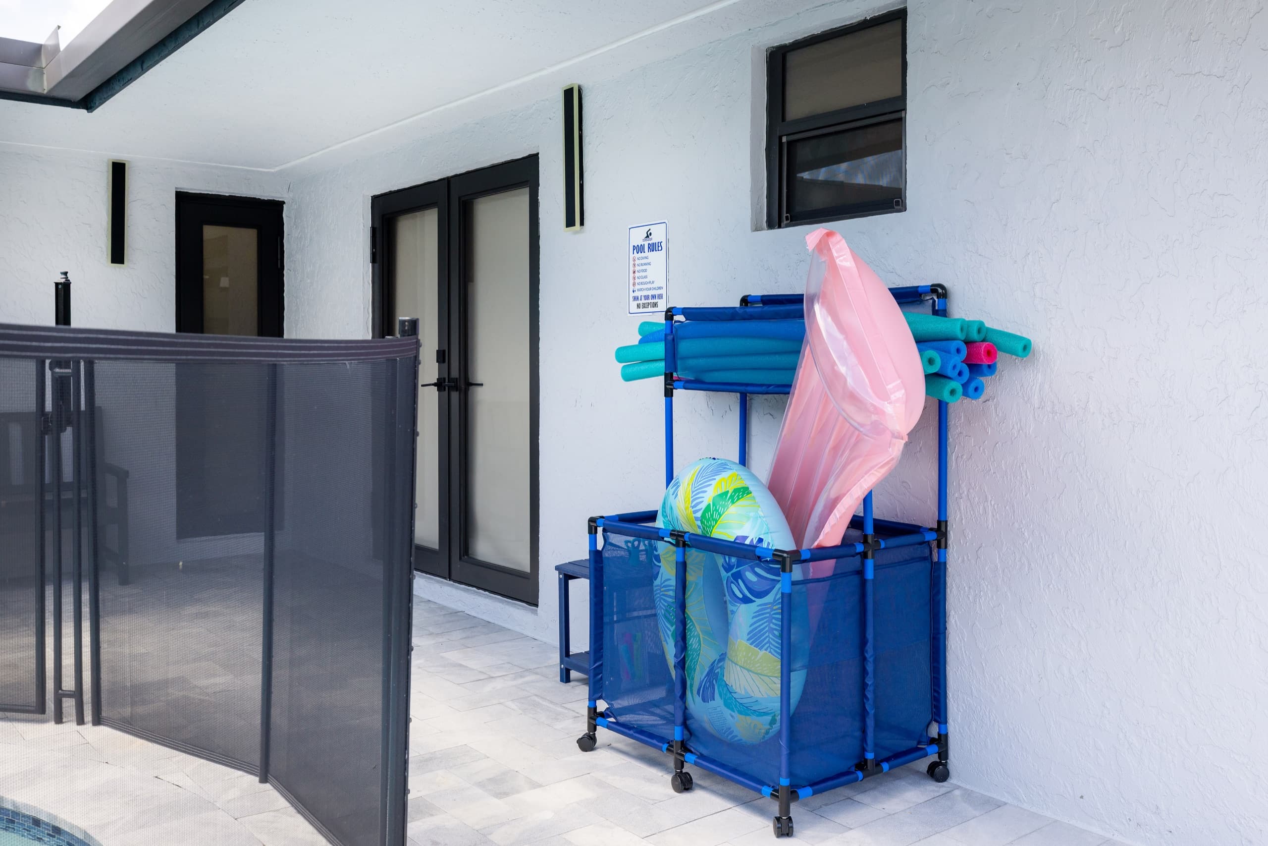Porch with a rack of pool toys and floats beside the glass doors.