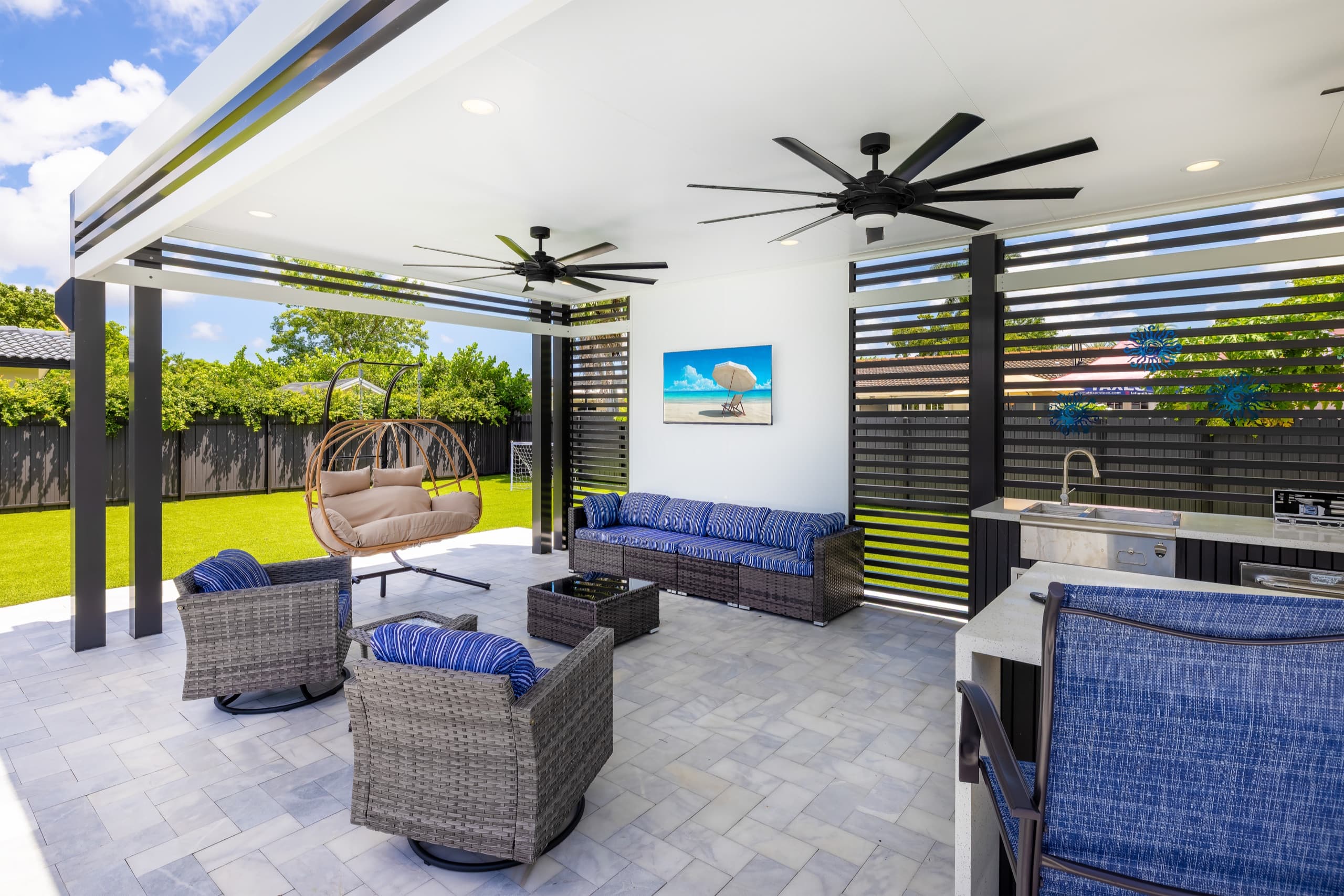 Pavilion lounge corner with a wicker sofa, armchairs, a hanging egg chair and a wall-mounted TV.