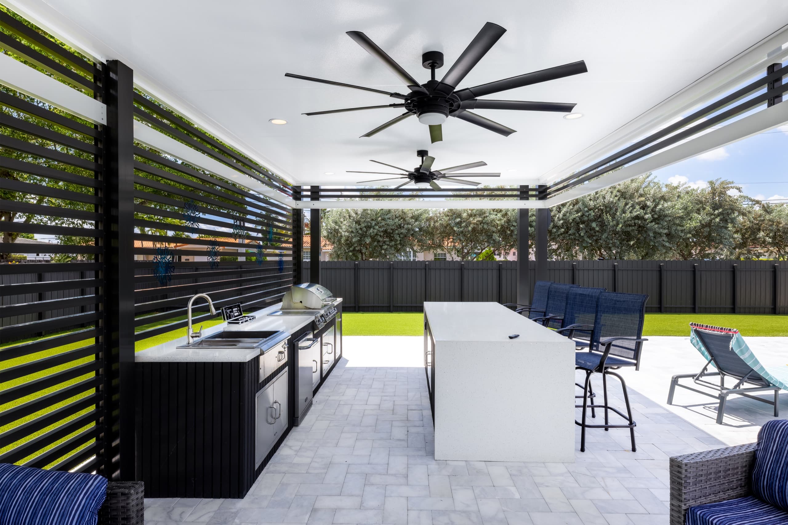 Inside the pavilion at the outdoor kitchen: a grill and sink along a slatted screen wall, with the bar island opposite.