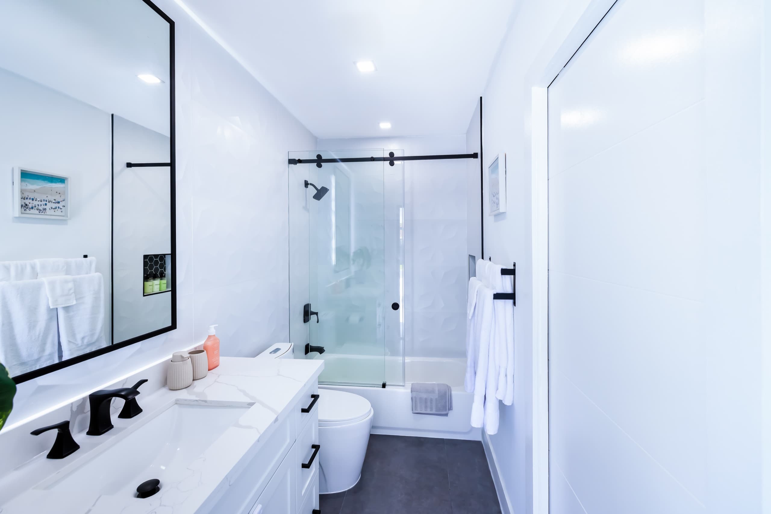 Narrow bathroom with a vanity, a toilet and a bathtub with a sliding glass panel at the far end.