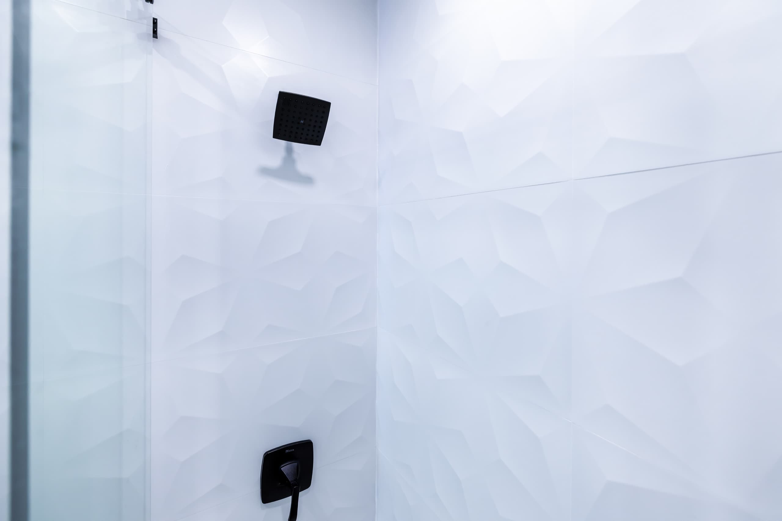 Textured white wall tiles with a black square shower head.