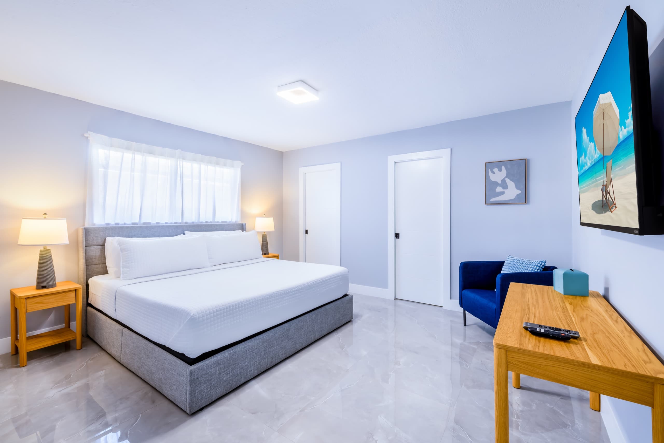 Bedroom with the grey king bed, a cobalt armchair, a desk and a wall-mounted TV.