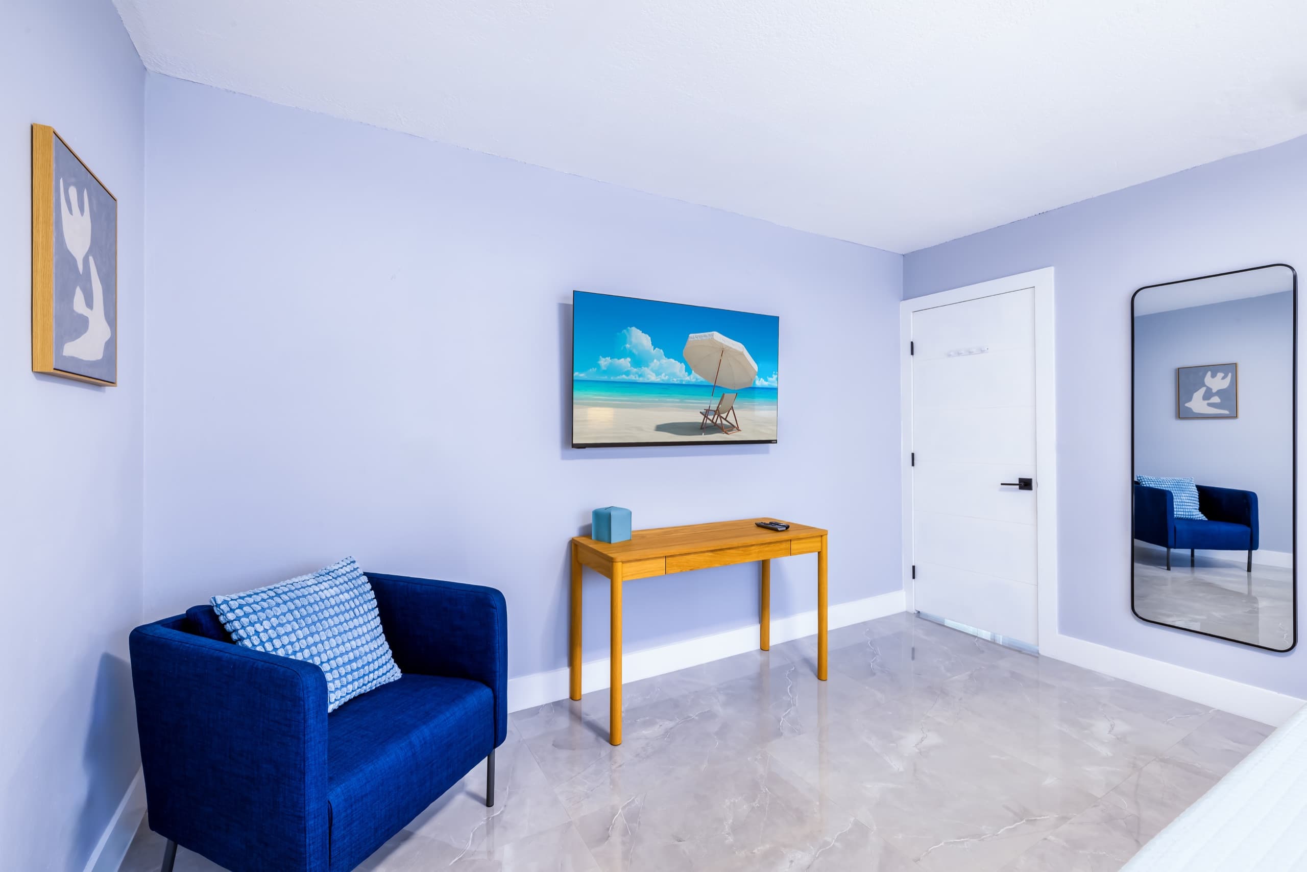 Cobalt armchair and desk beneath the TV, with the bedroom door and a full-length mirror.