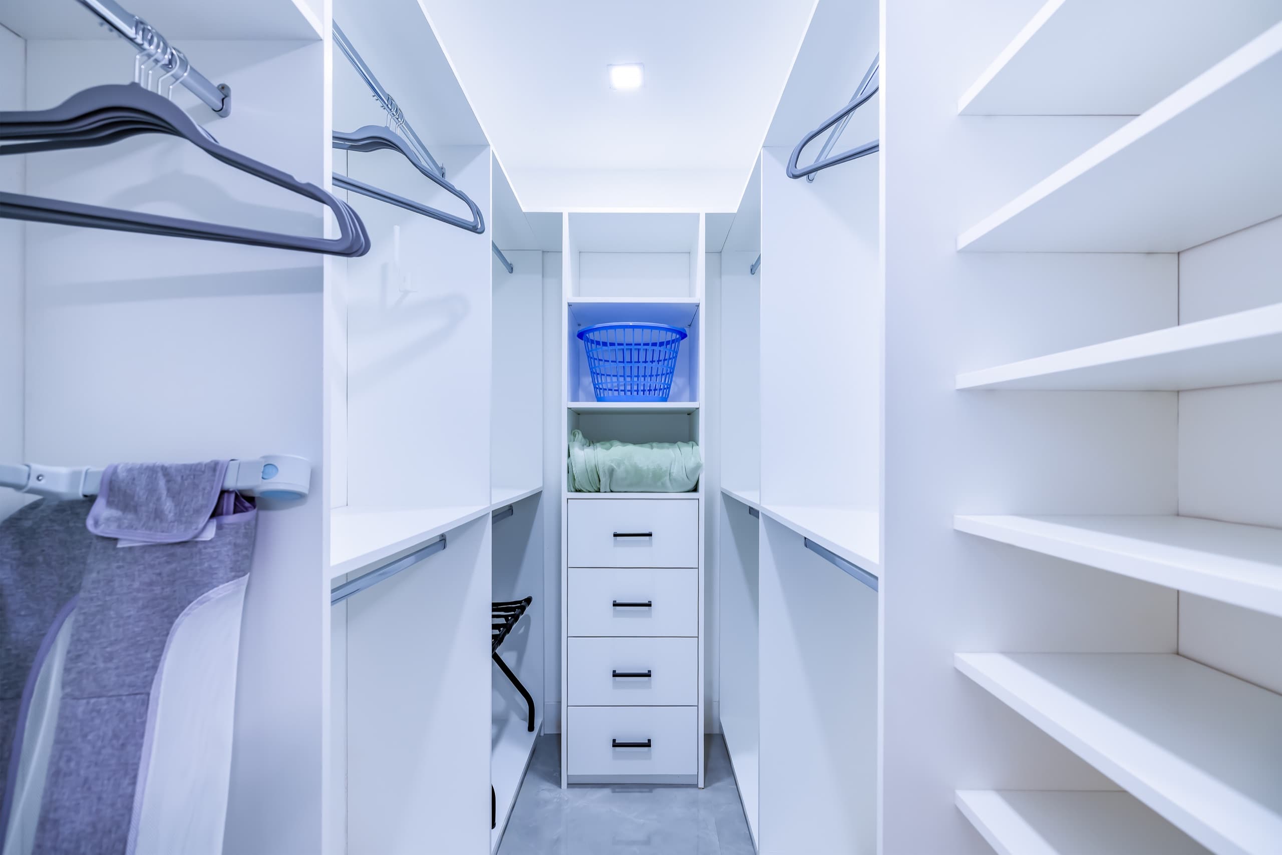 Closet with hanging rods and hangers, open shelves and a column of drawers.
