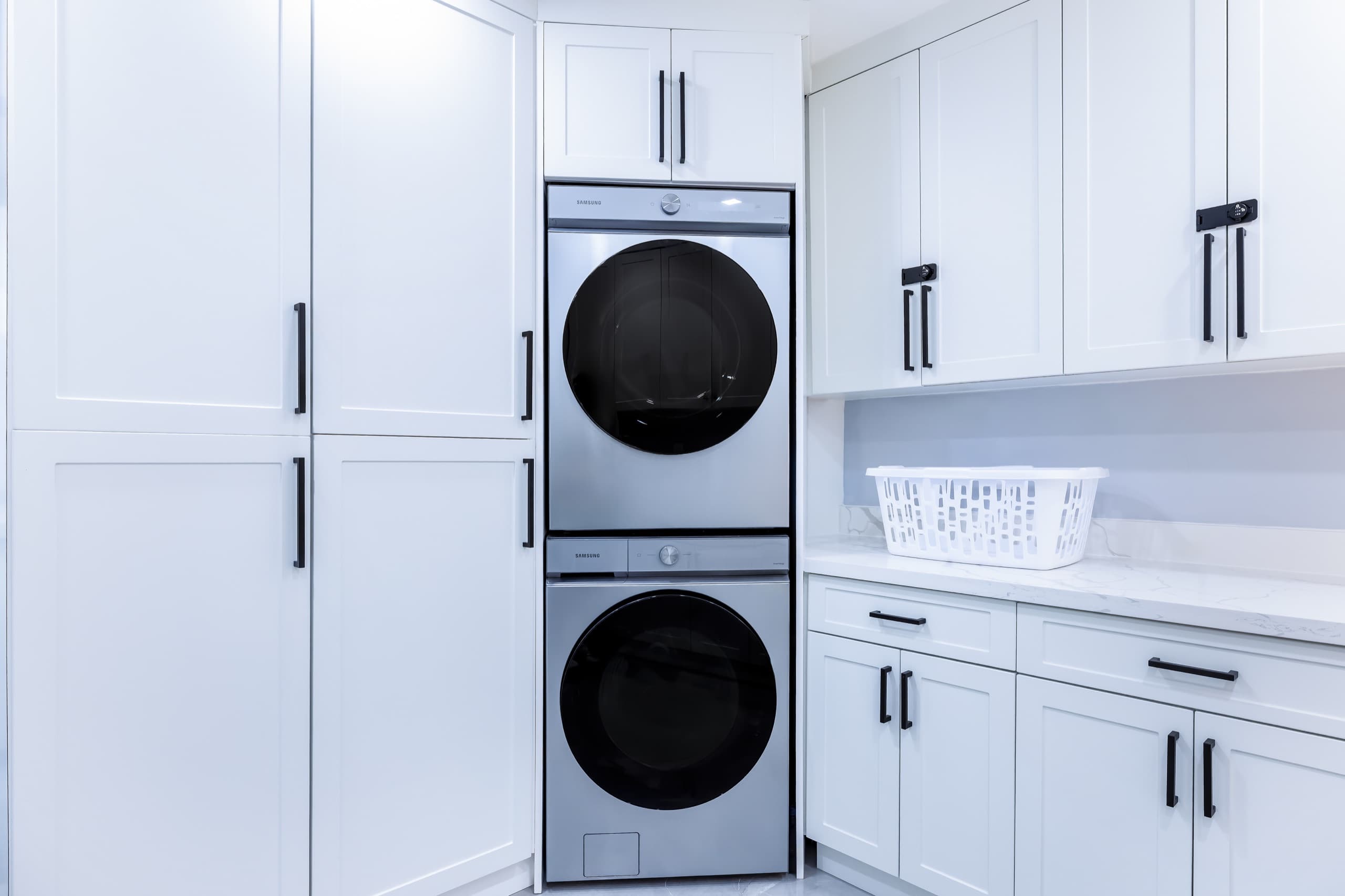 Stacked washer and dryer built into white cabinetry, with a laundry basket on the counter.