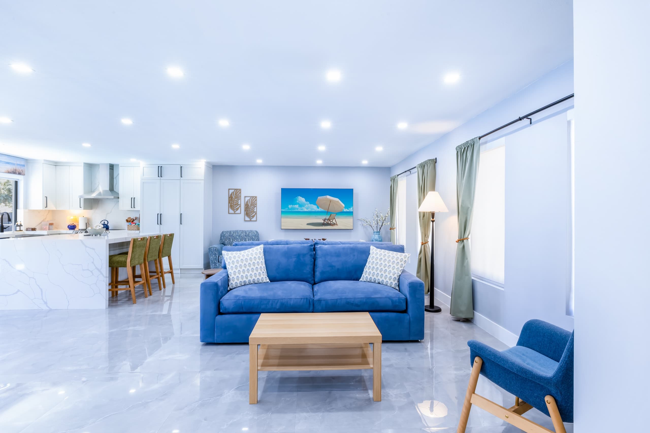 Blue sofa and coffee table centred in front of the TV wall, with the kitchen island to the left.