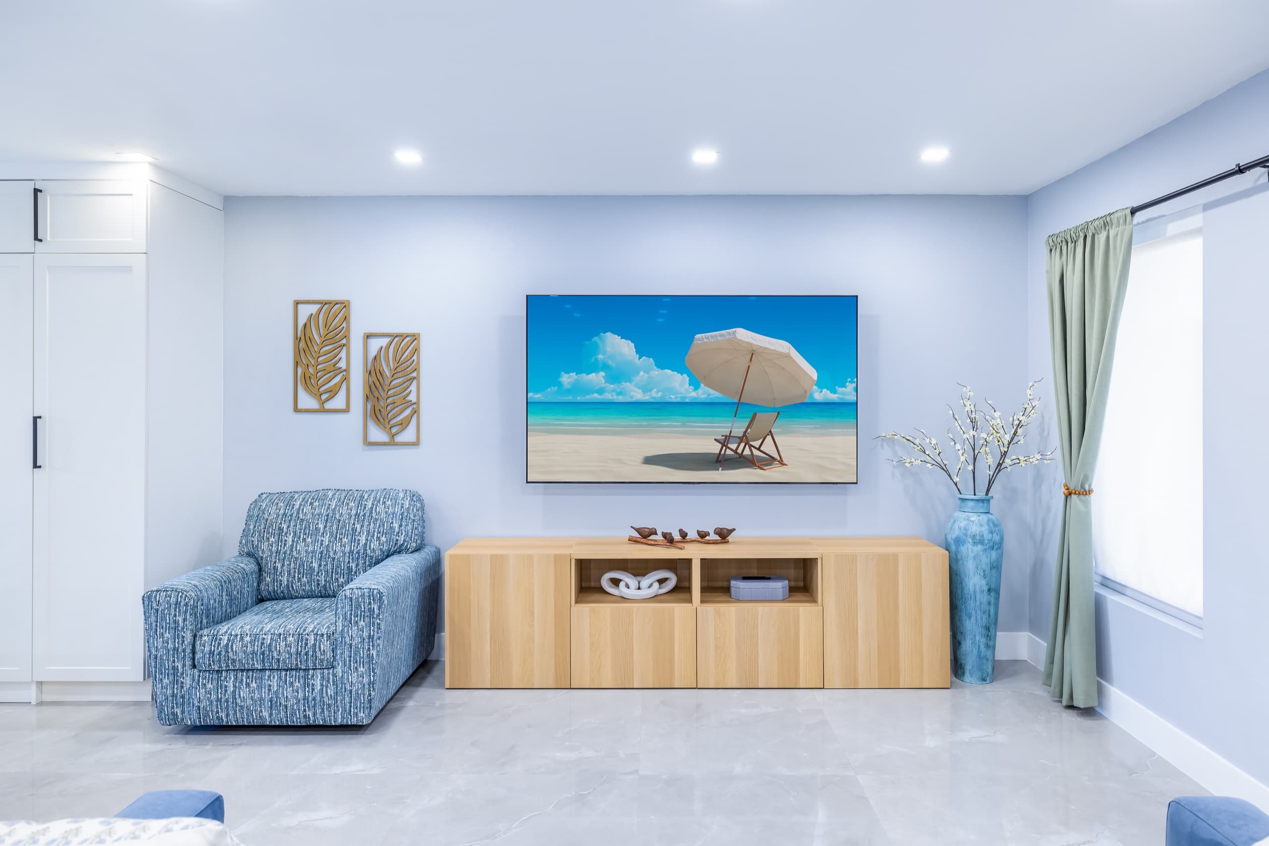 TV wall with a wooden media console, a blue patterned armchair and a tall teal vase.